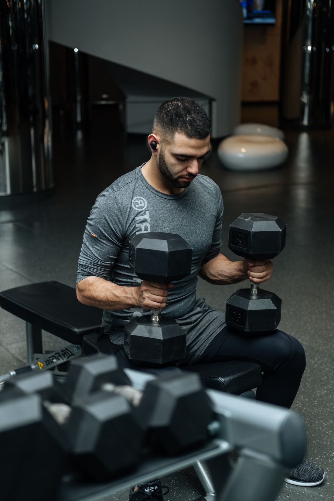 Man seated on a bench holding two dumbbells